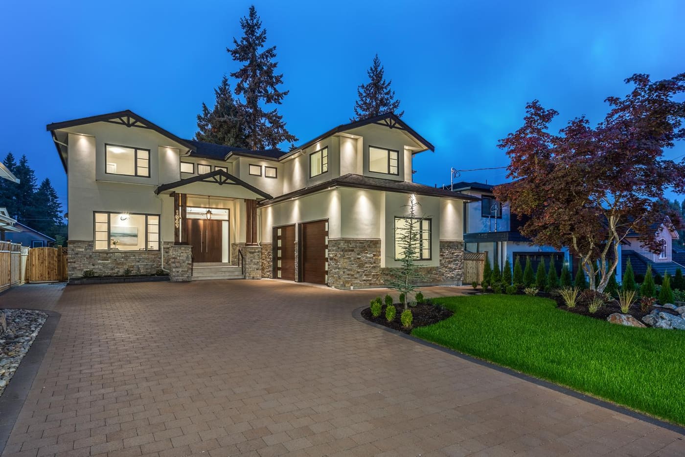 Two-storey home lit at dusk with stone-faced columns and a wide paver driveway