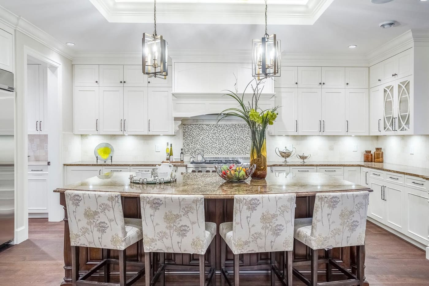White kitchen with a granite island, lantern pendants, and upholstered bar stools